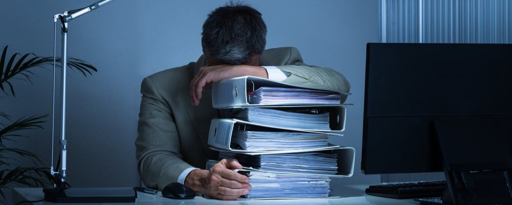 Uomo stanco che dorme sopra dei faldoni portadocumenti