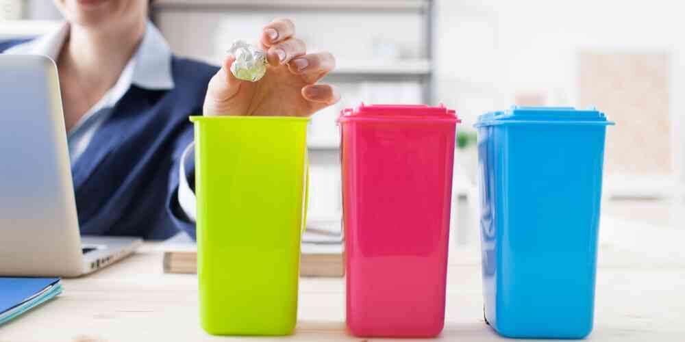 Piccoli bidoni della raccolta differenziata e donna che ricicla la carta in uno di essi