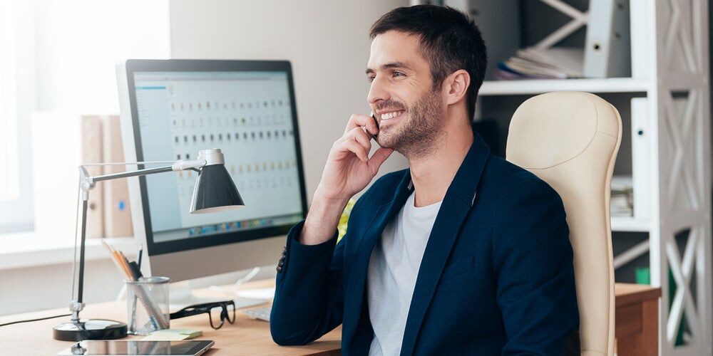 Ragazzo vestito in modo elegante parla al telefono alla scrivania e sorride
